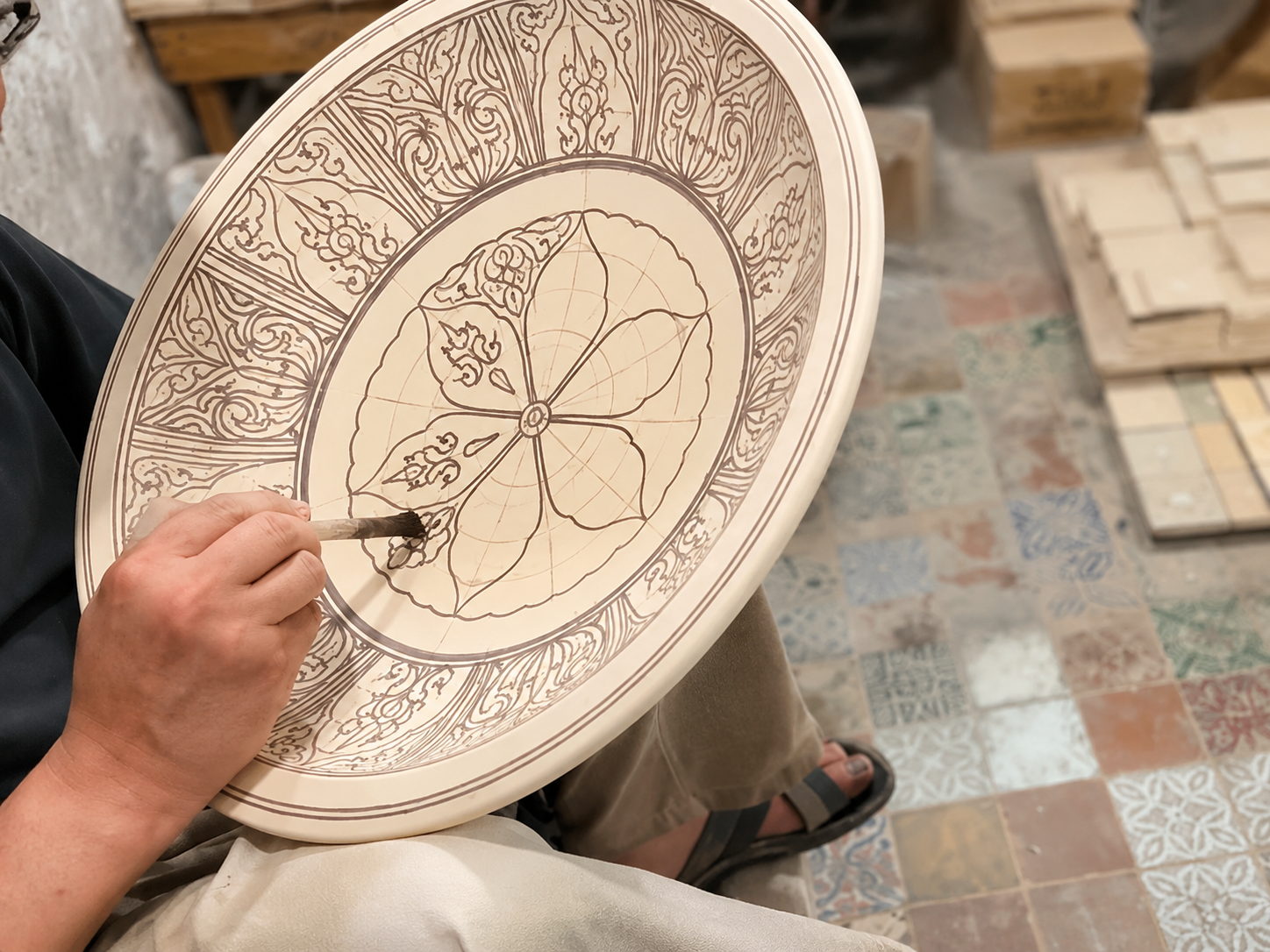 Hands drawing decorative pattern lines onto a ceramic plate.
